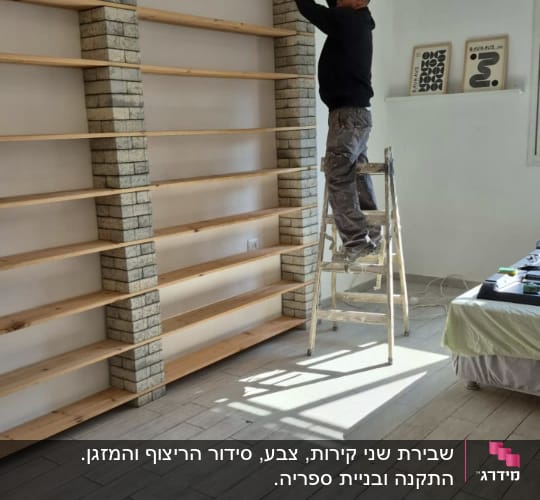 אדם על סולם מתקין מדפים בחדר עם רצפת עץ